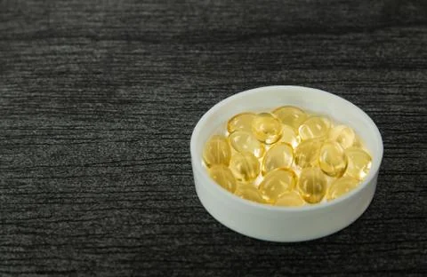 Yellow soft shell D-vitamin capsule in bowl. Fish oil capsules with omega 3 a Stock Photos
