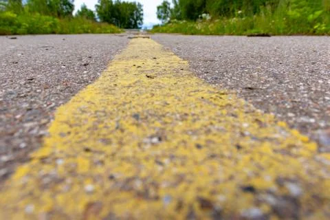 Yellow solid line, grunge road marking on asphalt close up with rural landsca Stock Photos