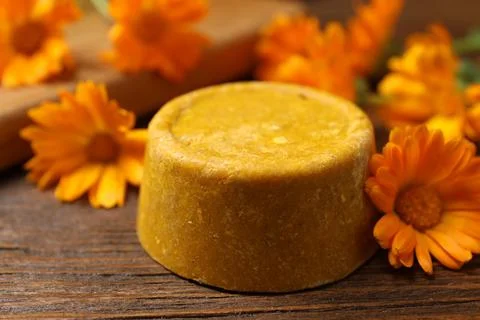 Yellow solid shampoo bar and flowers on wooden table, closeup. Hair care Foto stock