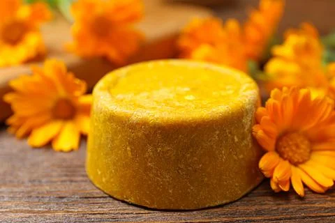 Yellow solid shampoo bar and flowers on wooden table, closeup. Hair care Foto stock