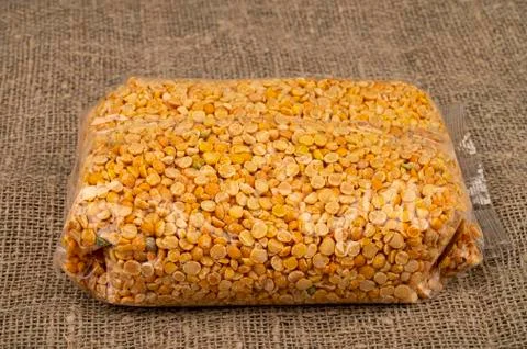 Yellow split peas in a cellophane bag on a background of coarse-textured burl Stock Photos