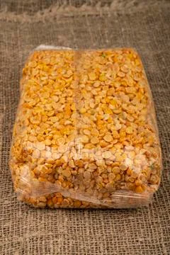Yellow split peas in a cellophane bag on a background of coarse-textured burl Stock Photos