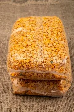 Yellow split peas in a cellophane bag on a background of coarse-textured burl Stock Photos