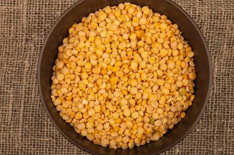 Yellow split peas in a ceramic bowl on a background of coarse-textured burlap Stock Photos