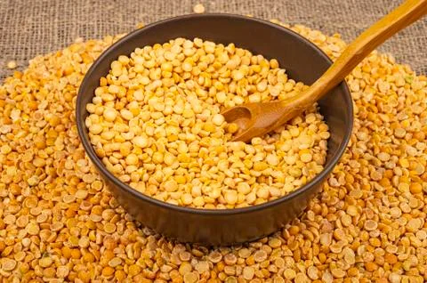 Yellow split peas in a ceramic bowl and grits scattered on a background of co Stock Photos