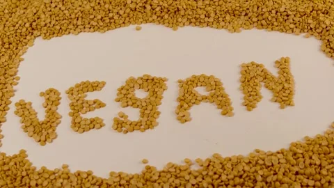 Yellow split peas form the word VEGAN on a seamless white surface. Stock Footage 309639845