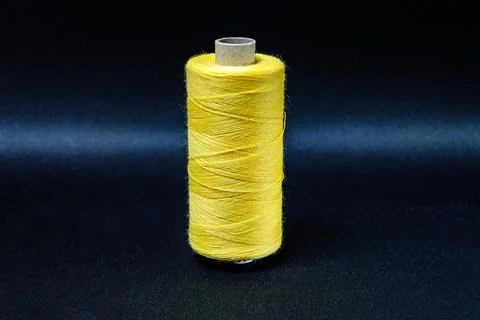 Yellow spool of thread on black background Foto stock