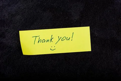 A yellow sticky note displaying the word Thank you on a textured stone dark b Stock Photos
