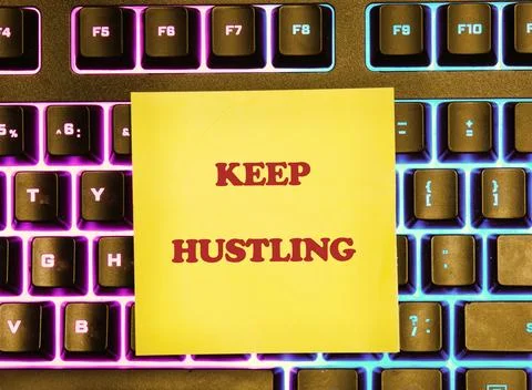 Yellow sticky note with KEEP HUSTLING in red bold text rests on a black compu Stock Photos