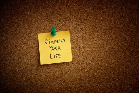 A yellow sticky note with the phrase Simplify Your Life written on it pinned Stock Photos