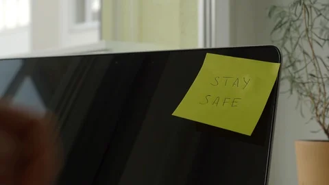 Yellow sticky note with "Stay Safe" text being sticked to laptop display Stock Footage 127656354