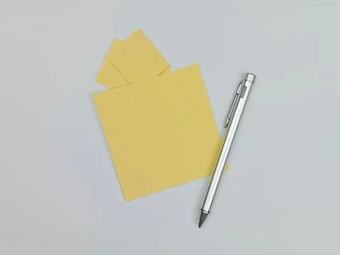 Yellow sticky notes and silver pen on white background Stock Photos