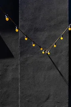 Yellow string lights on dark textured wall at daytime Stock Photos