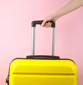 Yellow suitcase with handle held by hand against pink background Photos