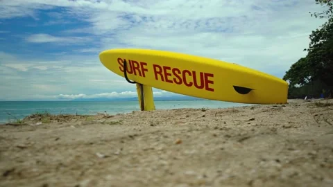Yellow surfboard on beach with red text surf rescue emergency on a beach Stock Footage 146486690