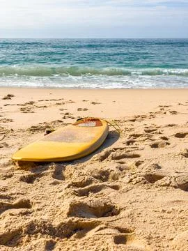 Yellow Surfboard Resting on Sandy Beach by Ocean Waves Stock Photos