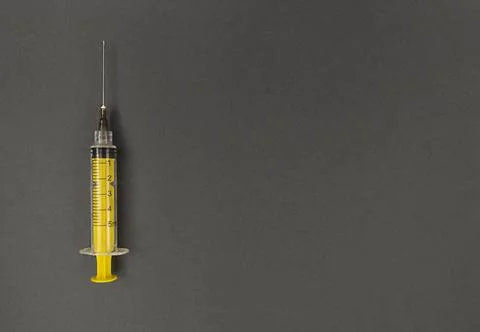 Yellow syringe on grey background. Simple flat lay with copy space. Stock Photos
