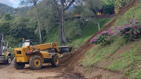 Yellow telescopic handler clearing mud landslide on a rural road Stock Footage 345101342