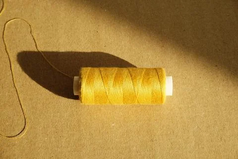 Yellow thread spool in direct sunlight on a craft background, sewing concept Stock Photos