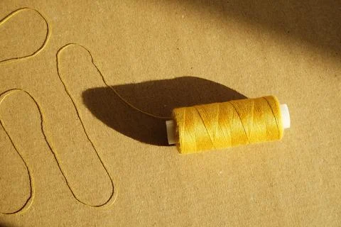 Yellow thread spool in direct sunlight on a craft background, sewing concept Stock Photos