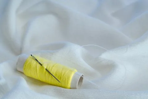 Yellow thread spooll with sewing needle on white cotton cloth Stock-Fotos