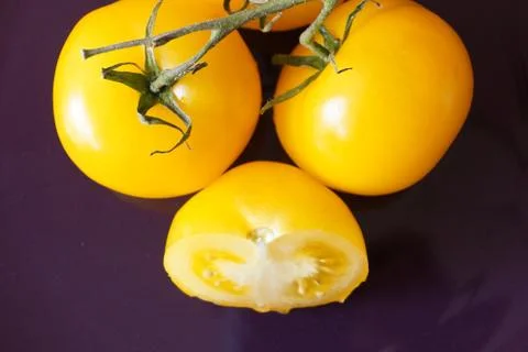 Yellow tomatoes on a dark background two of whole fruit and one cut in half frui Stock Photos