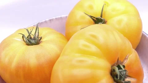Yellow tomatoes rotating in deep plate on white background Видео 344054182