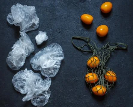 Yellow tomatoes in a string bag and plastic bags on a black background, a con Stock Photos