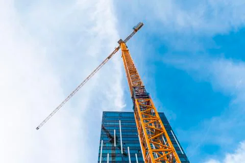 Yellow tower crane. Bottom view of a tall construction crane next to a modern Stock Photos