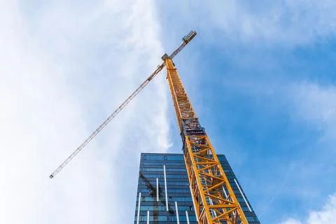 Yellow tower crane. Bottom view of a tall construction crane next to a modern Stock Photos