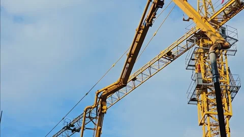 Yellow tower crane with concrete pump arm and pipes against blue sky. Stock Footage 297615751
