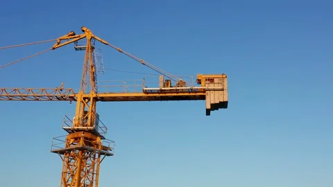 Yellow tower crane on a construction site, against clear blue sky Stock Footage 128186707