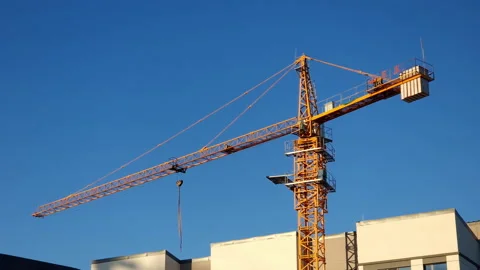 Yellow tower crane on a construction site, against clear blue sky, illuminated Stock Footage 232328290