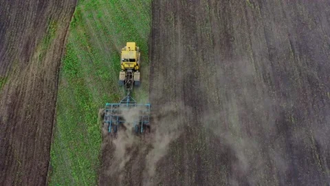 A yellow tractor with a blue plow plows the soil. Stock Footage 139855607