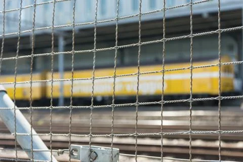 Yellow train seen through iron fence with railtracks Stock Photos