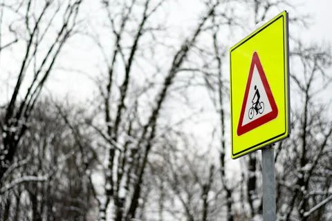 Yellow triangular bicycle warning sign on snow covered roadside Stock Photos