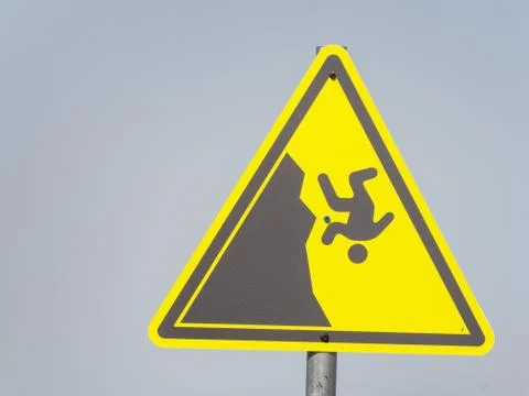 Yellow triangular sign with a man falling from a cliff on a gray background Stock Photos