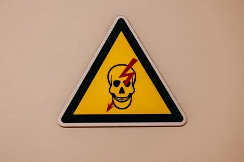 Yellow triangular warning sign with a skull and lightning bolt symbol Stock Photos
