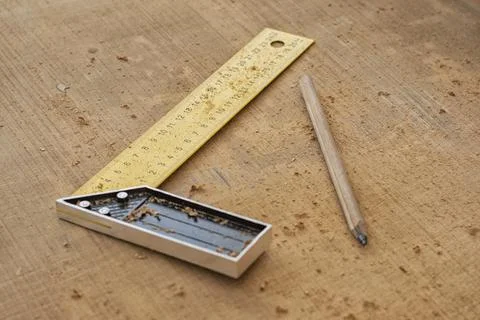 Yellow try square ruler and carpenter pencil on wooden board with sawdust. Wo Stock Photos