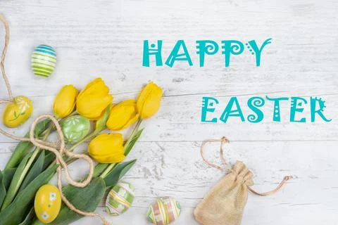Yellow tulips, easter eggs, canvas bag of gifts on a wooden surface. Easter c Stock Photos