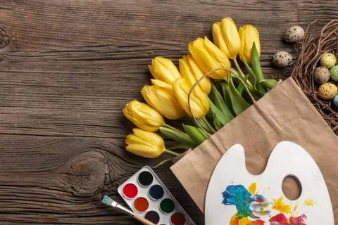 Yellow tulips, a nest with Easter eggs, bright colors and a palette on a wood Stock Photos