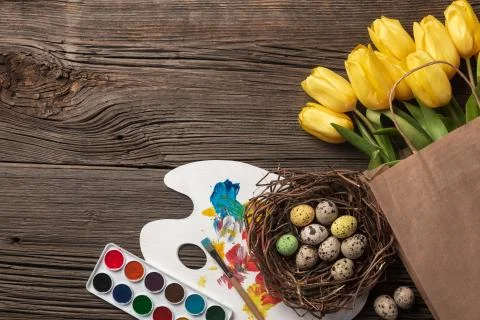 Yellow tulips, a nest with Easter eggs, bright colors and a palette on a wood Stock Photos