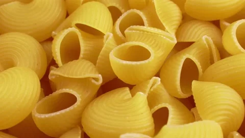 Yellow uncooked pipe rigate snail shape Italian pasta circle rotation close up Video stock 233997957