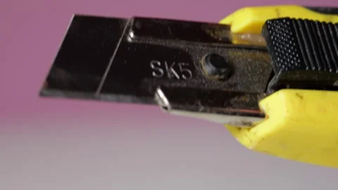 Yellow utility knife blade extending retracting housing pink background close up Stock Footage 320898217