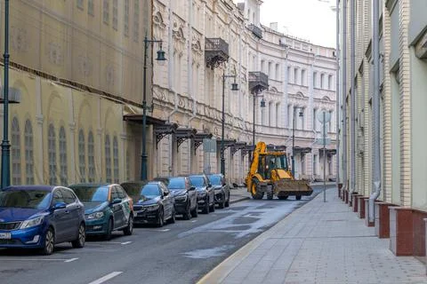 Yellow utility tractor driving down the street in the city Stock Photos