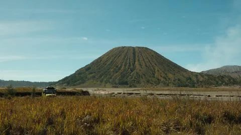 A yellow van is parked in a field next to a large volcano Stock Photos