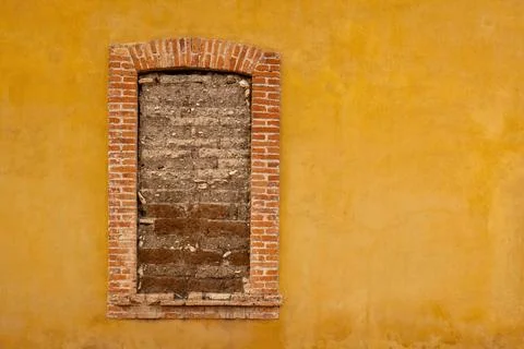 A yellow wall with a window that has a brick arch and a brick frame that sa.. Foto stock