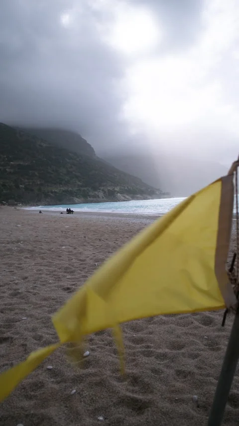 Yellow warning flag fluttering on an empty beach during a windy and overcast day Stock Footage 331158464