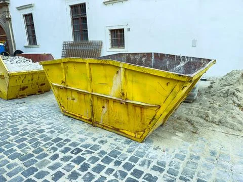 A yellow waste container is placed on the stone pavement in a construction ar Stock Photos