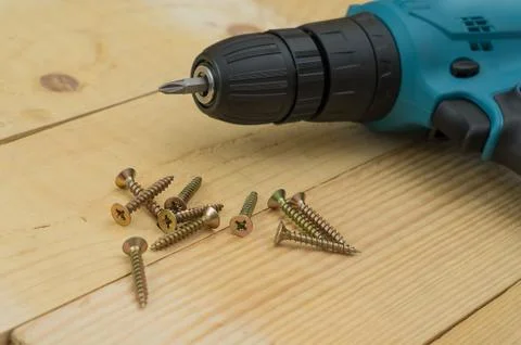 Yellow wood screws and electric drill lie on a wooden table Stock Photos